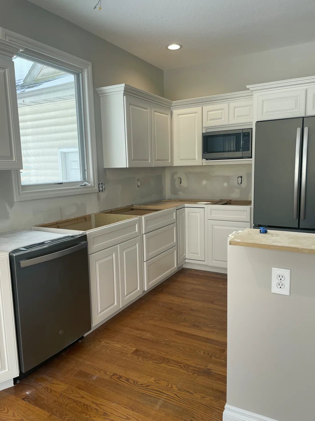 A galley kitchen finished in white with a stainless fridge and oak floor.