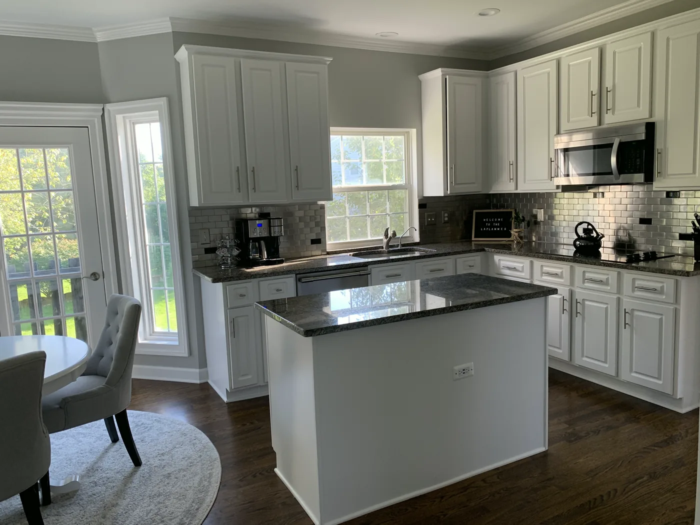 A finished white kitchen with a dark stone island, subway tile and a bay window.