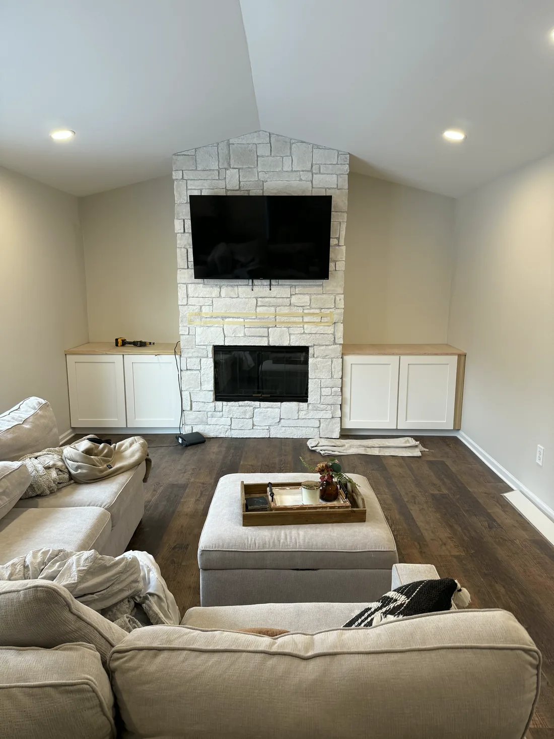 A finished family room: a white stone fireplace with a mounted television, a sectional and a dark wood floor.