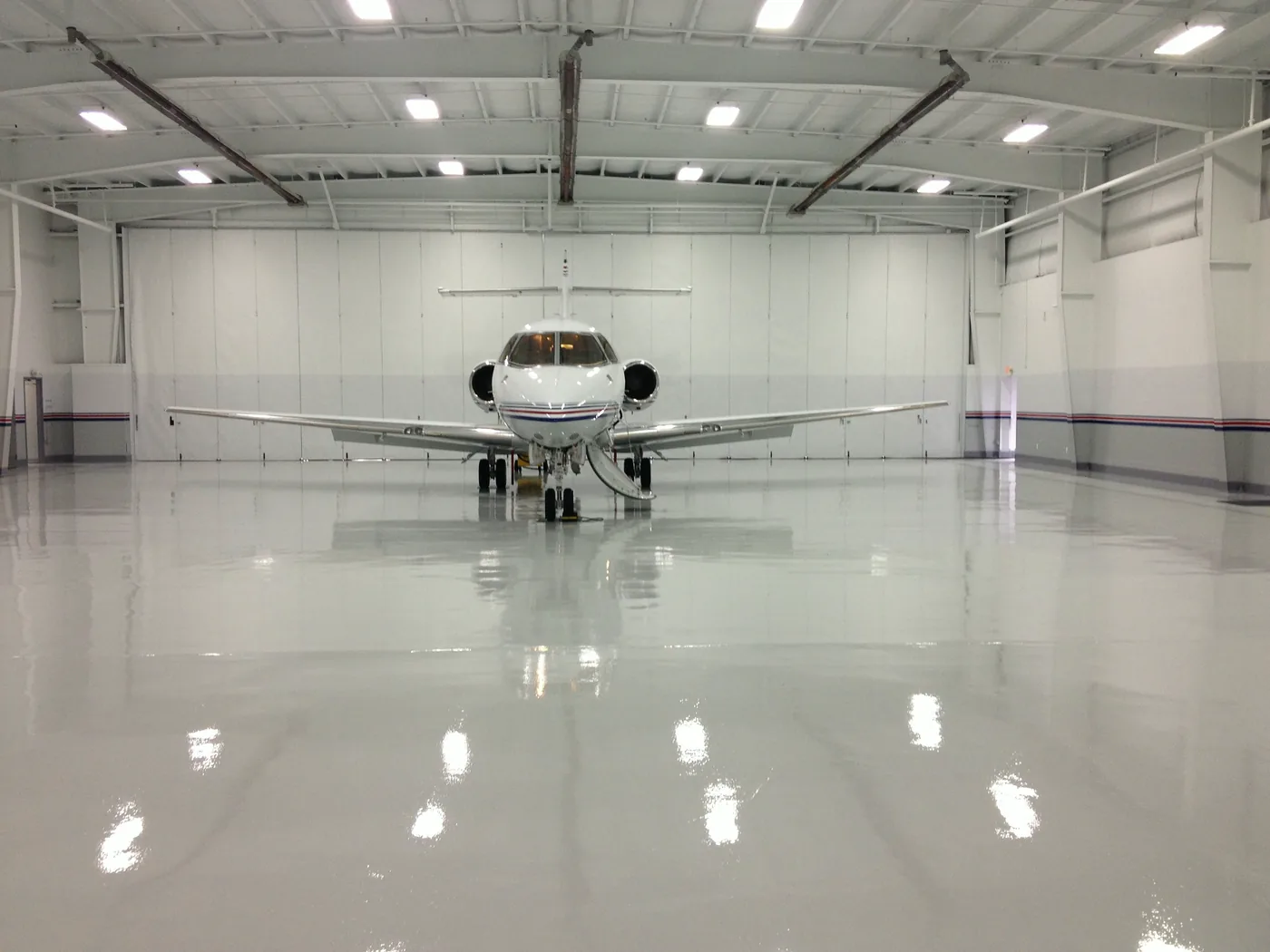 An aircraft hangar with a glossy pale floor reflecting the lights and a small jet.
