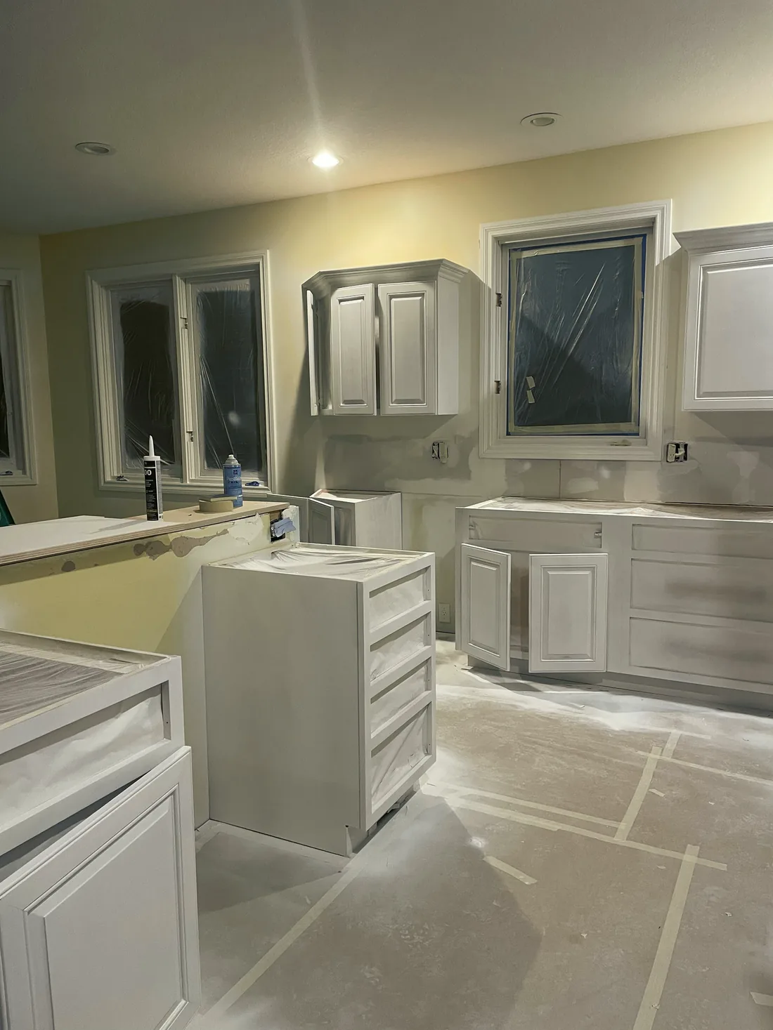 Kitchen cabinet boxes with the doors off, primed, the floor covered in paper.