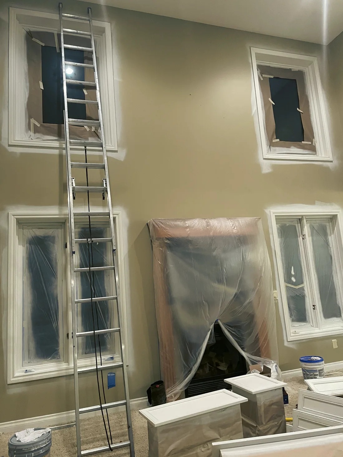 An extension ladder against a tall wall, windows masked, furniture under plastic sheeting.